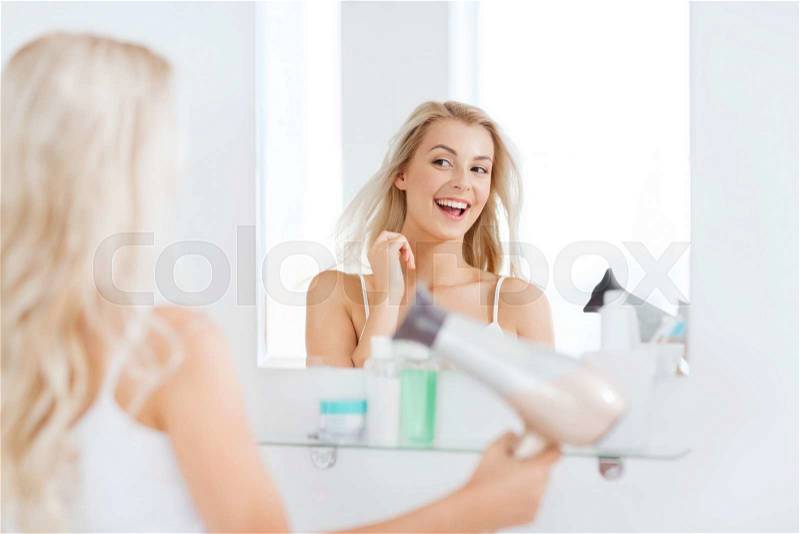 Beauty, hairstyle, morning and people concept - smiling young woman with fan blow drying her hair looking to mirror at home bathroom, stock photo