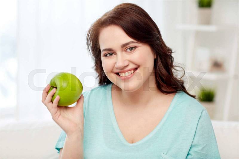 Healthy eating, organic food, fruits, diet and people concept - happy young plus size woman eating green apple at home, stock photo