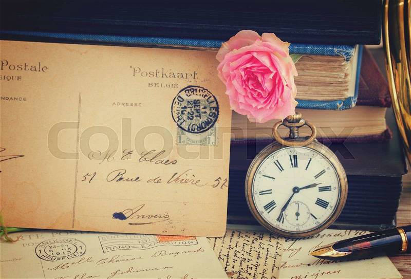 Antique pocket clock with postcard on vintage books and letters background, retro toned, stock photo
