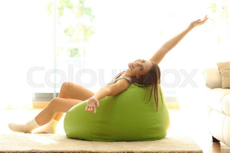 Happy girl stretching arms looking at camera and sitting on a pouf at home, stock photo