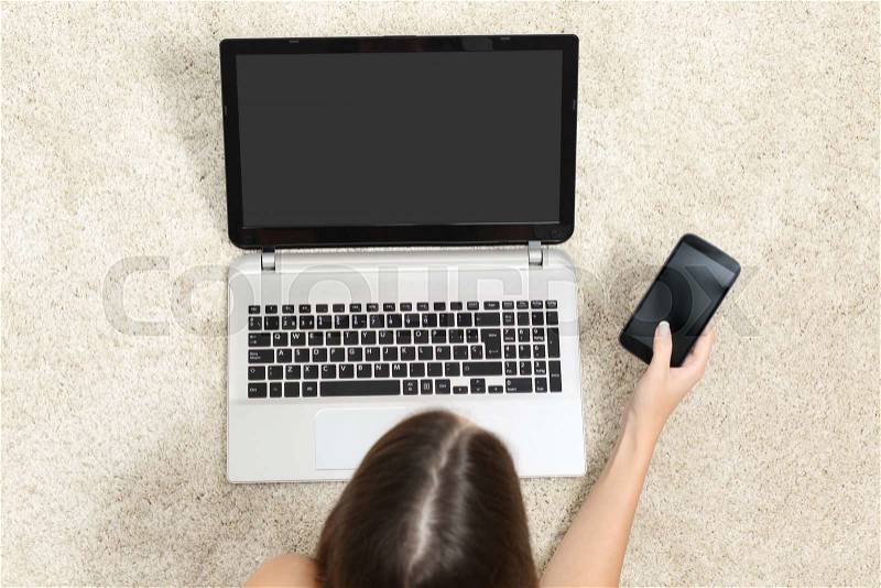 Top view of a girl working with a tablet and phone showing blank screens lying on a carpet at home, stock photo