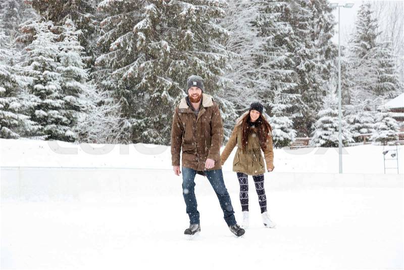 Smiling young couple ice skating outdoors with snow on background, stock photo