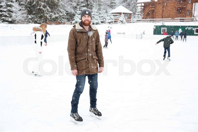 Smiling man ice skating outdoors with snow on background, stock photo
