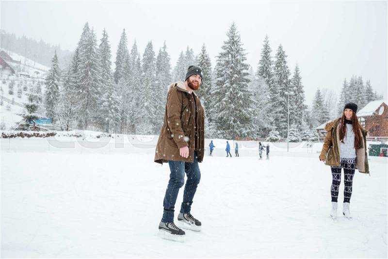 Smiling couple ice skating outdoors with snow on background, stock photo