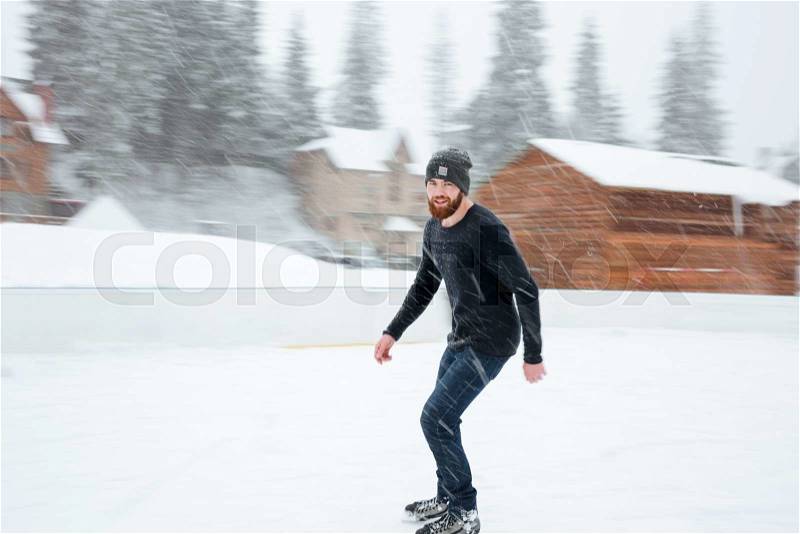 Happy man ice skating outdoors with snow on background, stock photo