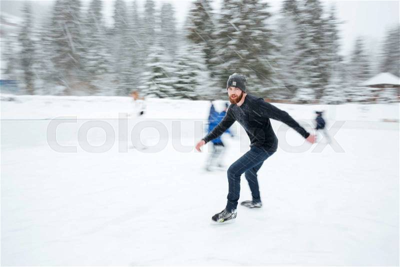 Handsome man ice skating outdoors with snow on background, stock photo