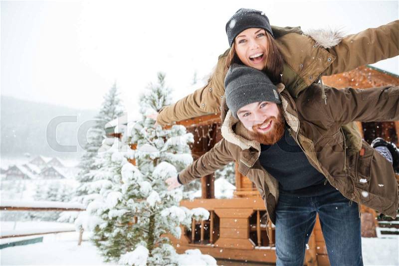 Happy handsome bearded man piggibacking his girlfriend and laughing in winter, stock photo
