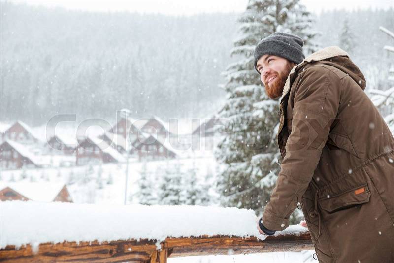 Smiling handsome bearded man standing and enjoying snowy weather on winter resort, stock photo