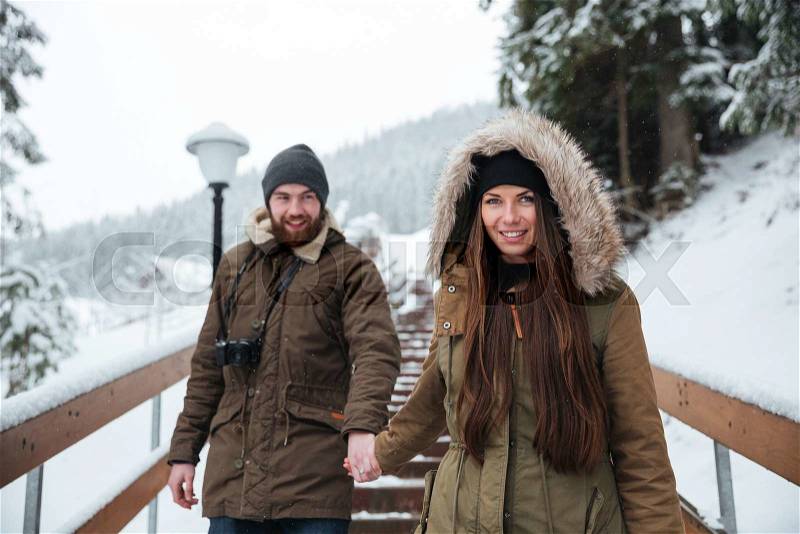 Smiling young couple holding hand and walking on stairs in winter mountains, stock photo