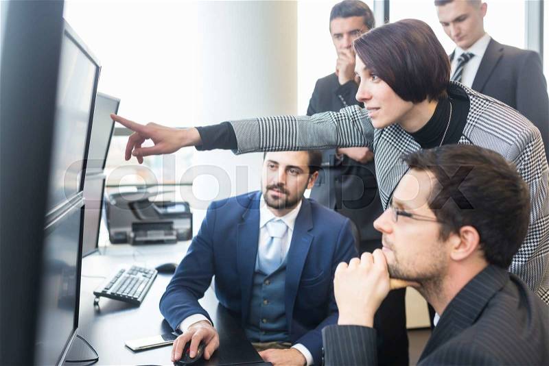Business team looking at data on multiple computer screens in corporate office. Businesswoman pointing on screen. Business people trading online. Business, entrepreneurship and team work concept, stock photo