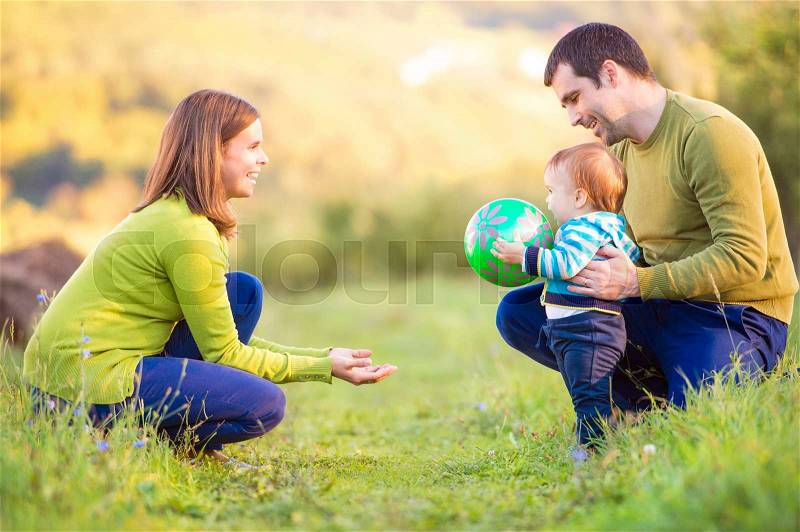 Mother and father holding their little son making first steps outside in green sunny nature, stock photo