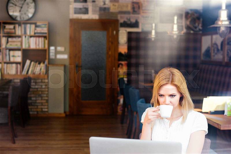 Blond woman with notebook in cafe sitting at the table drinking coffee, stock photo