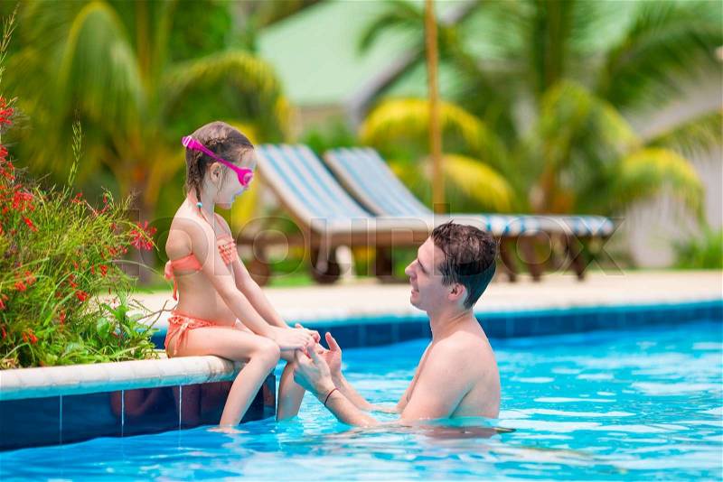 Little girl and happy dad having fun together in outdoors swimming pool, stock photo