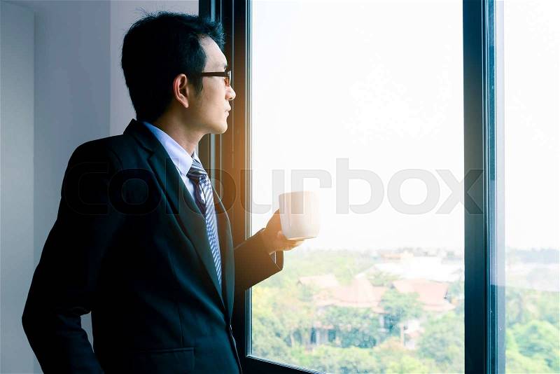 Businessman in glasses is drinking hot coffee by the window. , stock photo