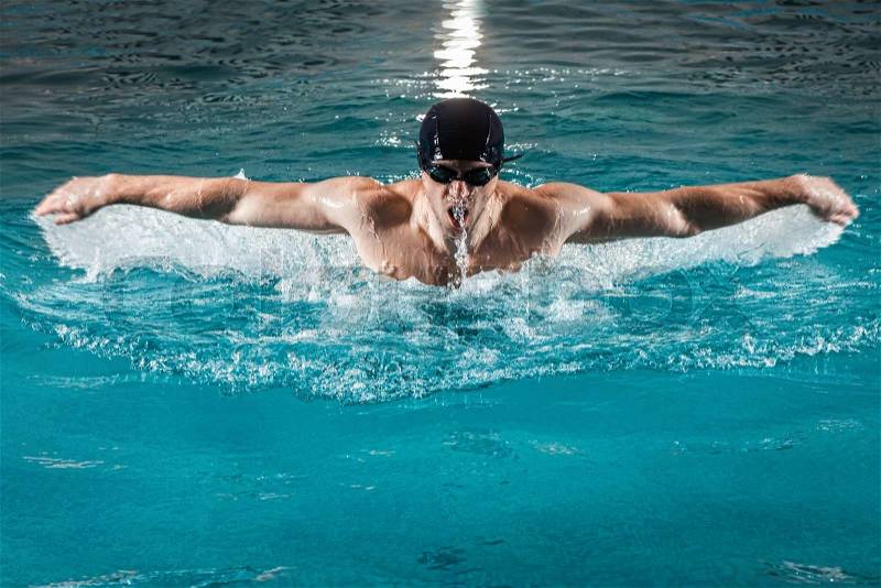 Muscular young man swims the butterfly in the pool, stock photo