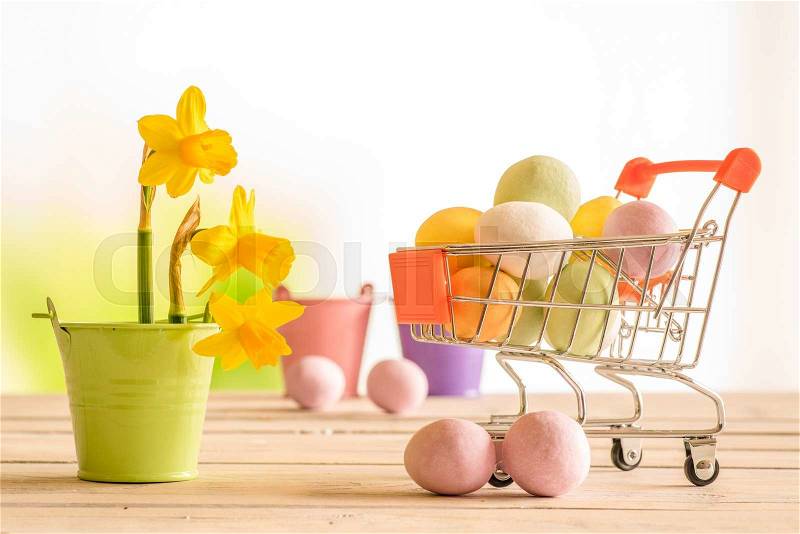 Shopping cart with colorful easter eggs and daffodils in a flowerpot, stock photo