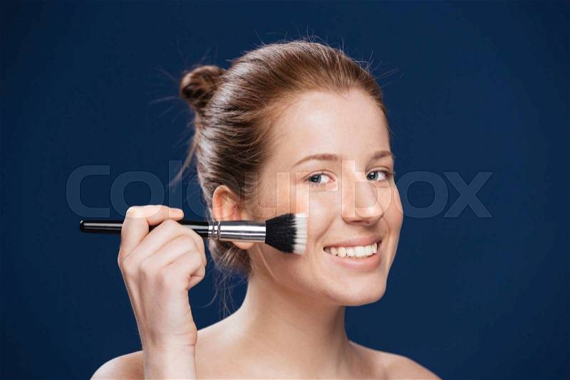 Smiling woman with cosmetic brush over blue background, stock photo