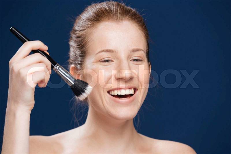 Laughing woman with cosmetic brush over blue background, stock photo