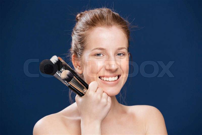 Smiling woman holding makeup brushes over blue background, stock photo