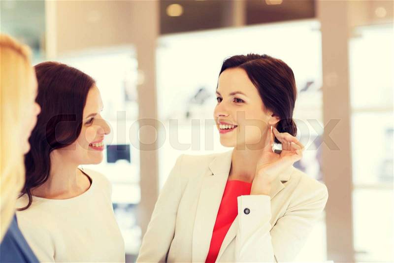 Sale, consumerism, shopping and people concept - happy happy women choosing and trying on earrings at jewelry store, stock photo