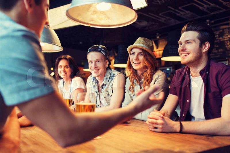 People, leisure, friendship and communication concept - group of happy smiling friends drinking beer and talking at bar or pub, stock photo