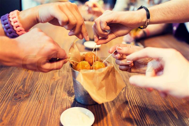 Fast food, junk food, unhealthy eating and culinary concept - close up of people hands taking cheese balls with skewers at bar or restaurant, stock photo