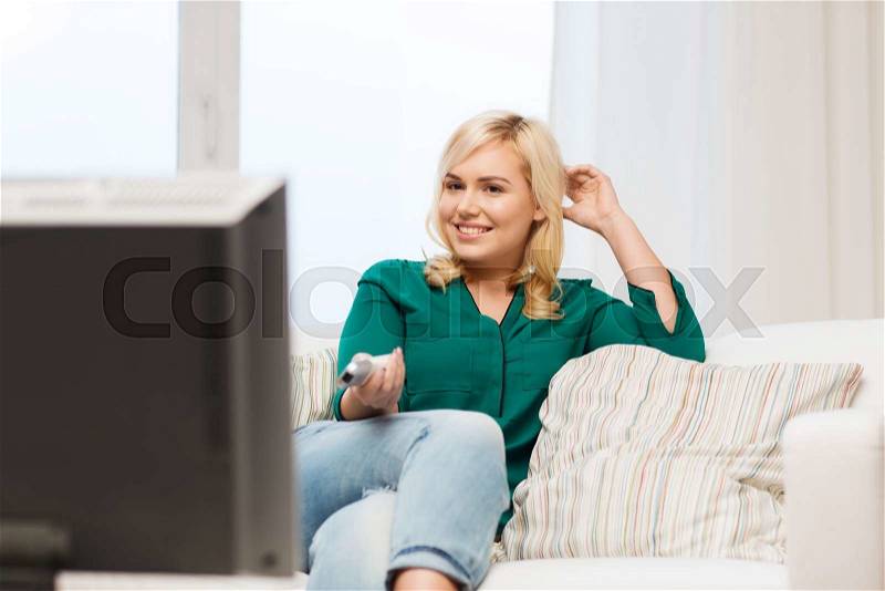 Television, leisure and people concept - smiling woman sitting on couch with remote control and watching tv at home, stock photo