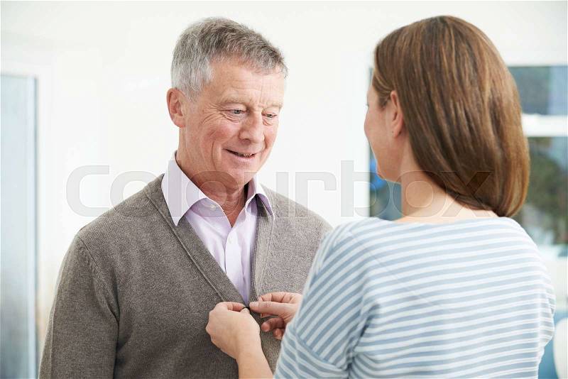 Adult Daughter Helping Senior Man To Button Cardigan, stock photo