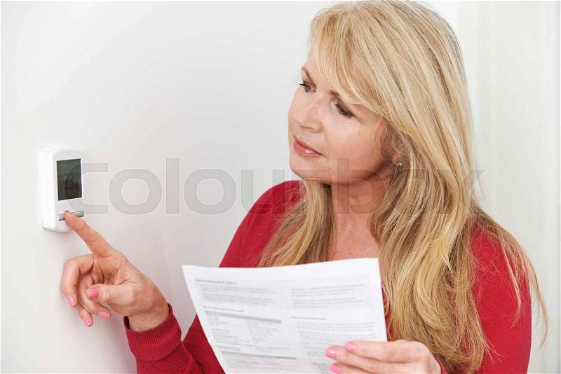 Worried Woman With Heating Bill Turning Down Thermostat, stock photo
