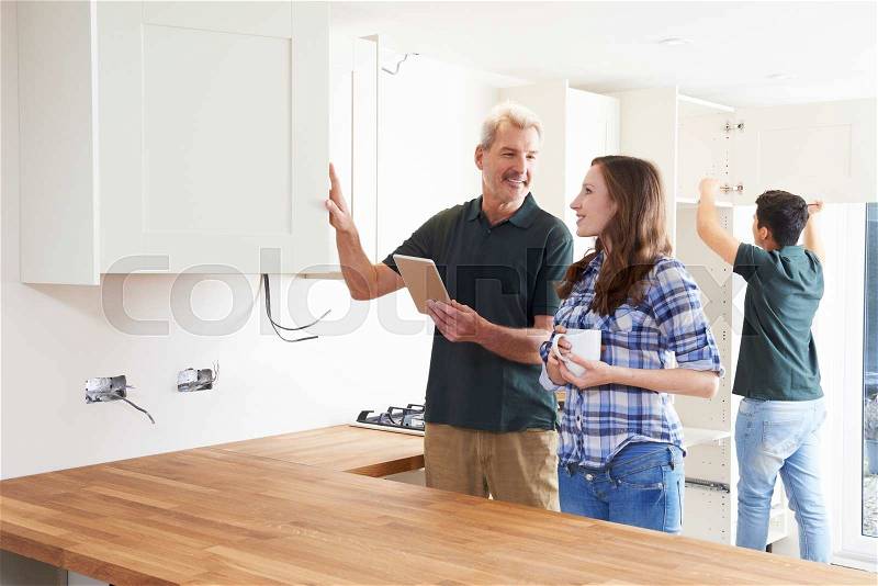 Woman With Carpenter Looking At Plans For Kitchen On Digital Tablet, stock photo