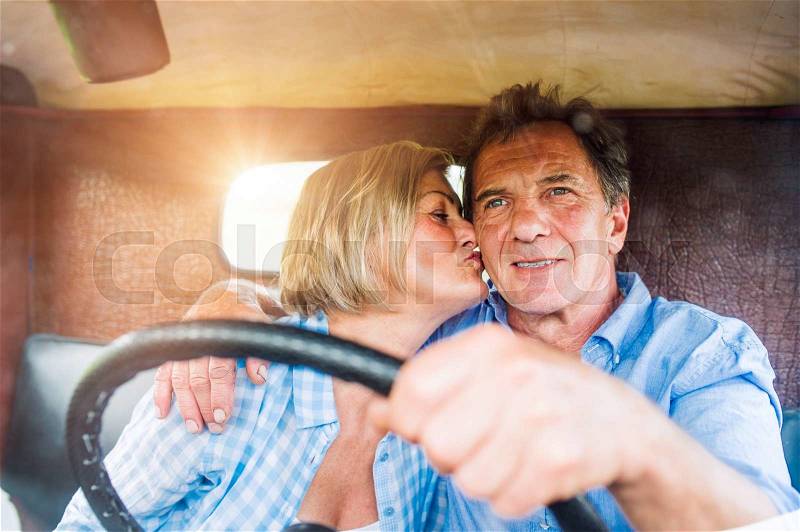 Close up of senior couple inside a pickup truck, man holding a steering wheel, woman kissing him, stock photo