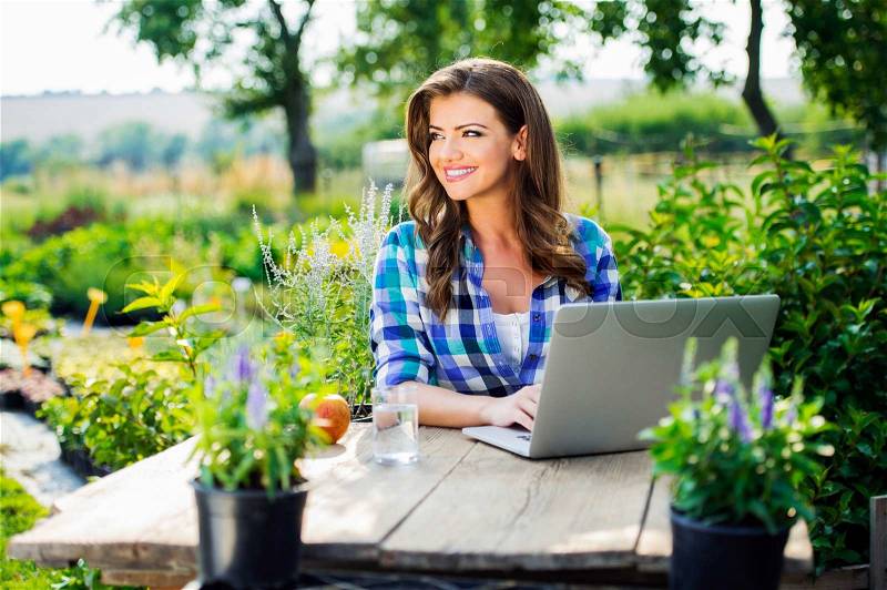 Beautiful gardener with notebook sitting at the table, managing supplies, green sunny nature, stock photo