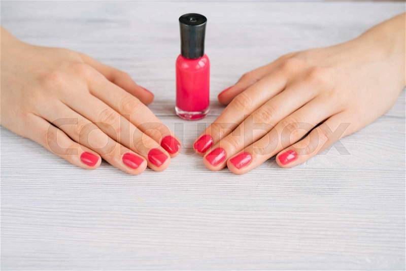 Female hands with red manicure and nail polish bottle on a wooden table, stock photo