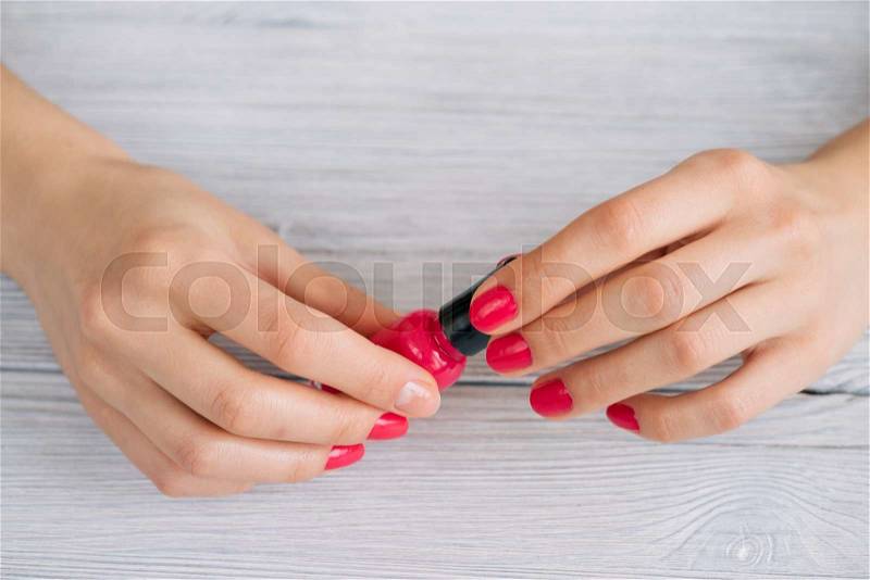 Female hands holding a bottle of red nail polish, stock photo