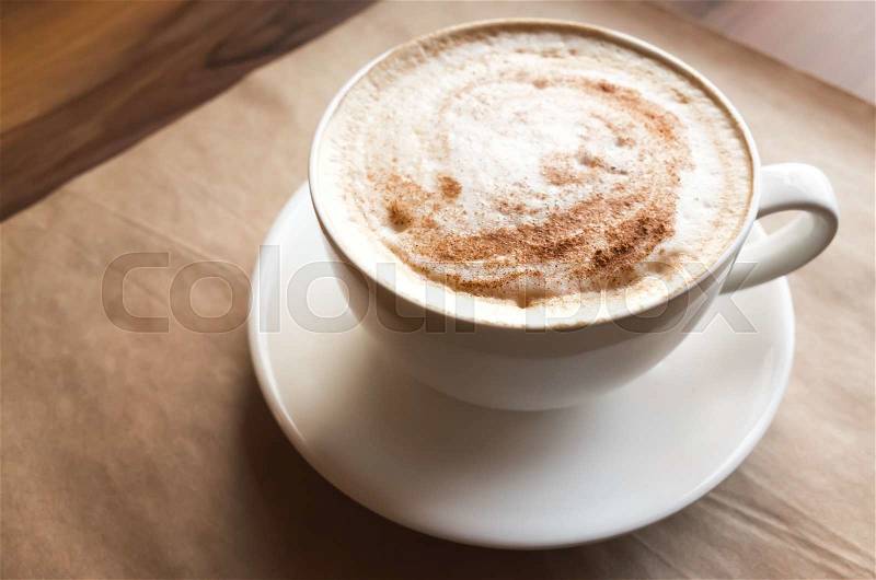 Cappuccino. Big cup of coffee with milk foam stands over old paper on wooden table in cafeteria, stock photo