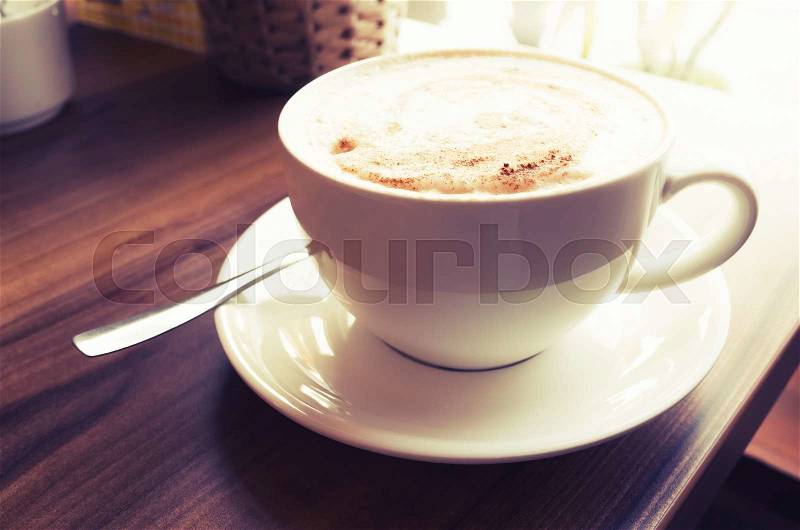 Cup of cappuccino. Coffee with milk foam stands on wooden table in cafeteria, vintage tonal correction photo filter, old style effect, stock photo