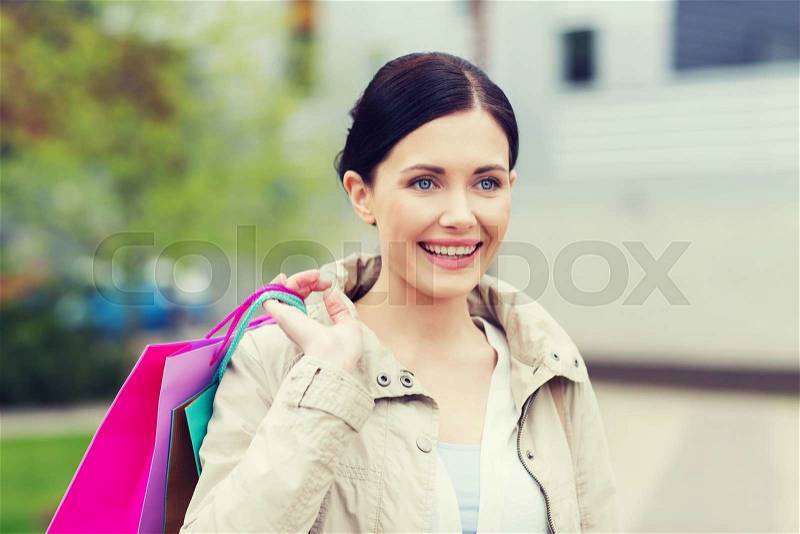 Consumerism, leisure and people concept - smiling woman with shopping bags coming from sale in park, stock photo