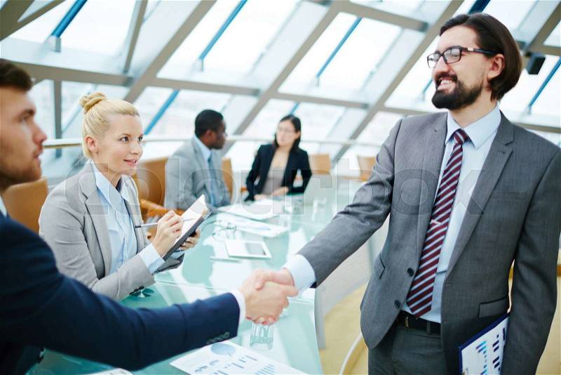 Young secretary looking at businessmen handshaking after introduction, stock photo