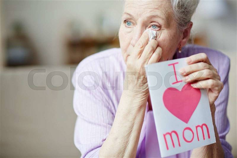 Elderly woman with greeting card wiping tears, stock photo