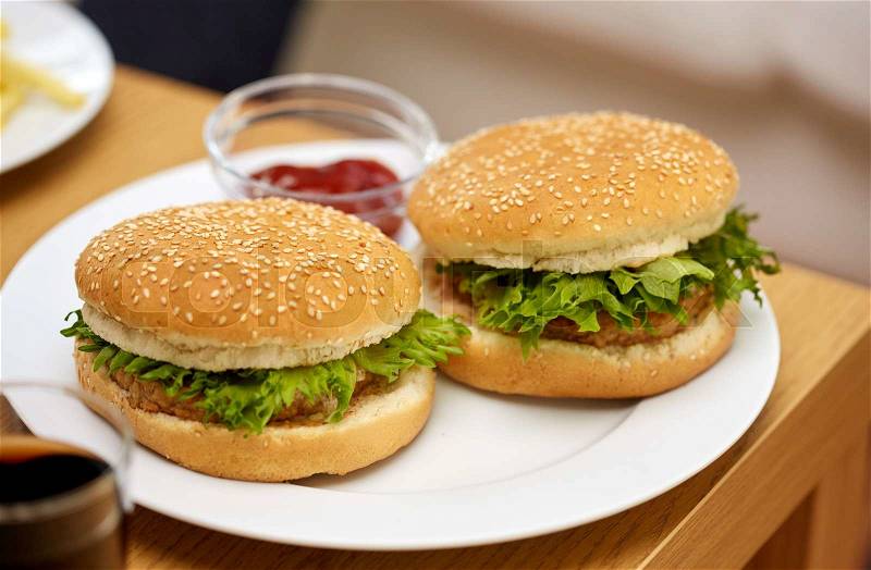 Fast food and unhealthy eating concept - close up of hamburgers on table with ketchup at fast food restaurant or home, stock photo
