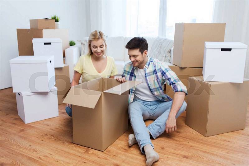 Moving, people, repair and real estate concept - smiling couple looking into big cardboard box at new home, stock photo