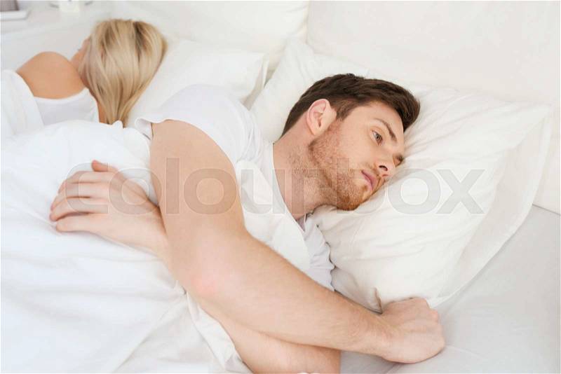 People, health, sleep disorder concept - couple lying back to back in bed at home and young man suffering from insomnia, stock photo