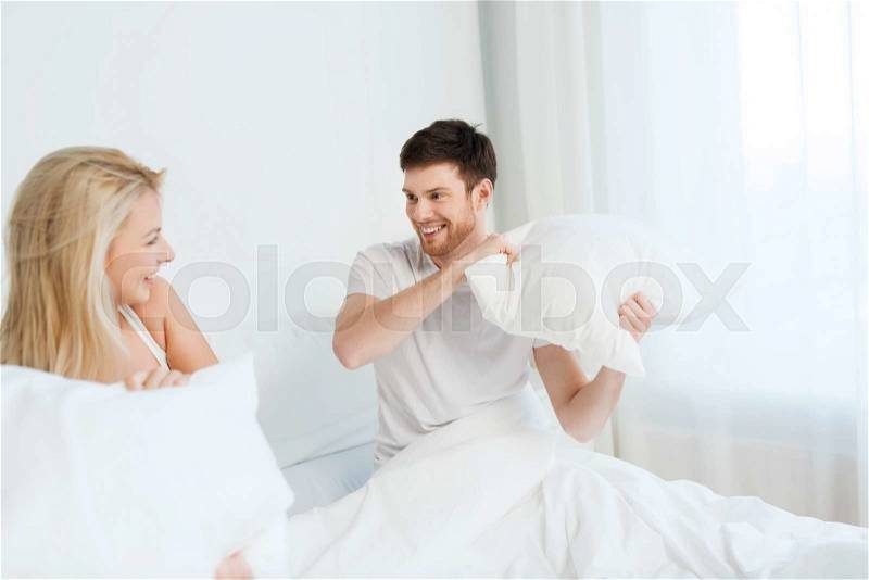 People, family, fun, bedtime and fun concept - happy couple having pillow fight in bed at home, stock photo