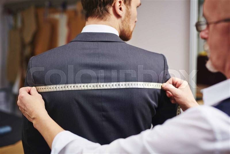 Mature tailor measuring back of jacket worn by his client, stock photo