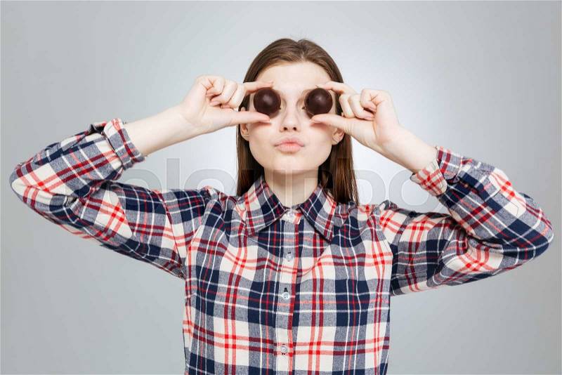 Beautiful amusing teenage girl in checkered shirt covered her eyes with round chocolate candies, stock photo