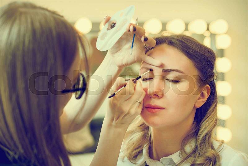 Make-up artist applying makeup on model\'s face, stock photo