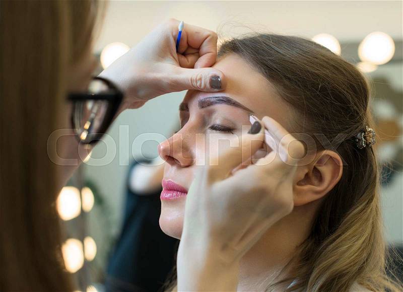 Make-up artist tweezing eyebrow on model\'s face, stock photo