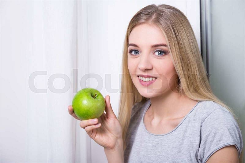 Portrait of young woman holding green apple at home, stock photo