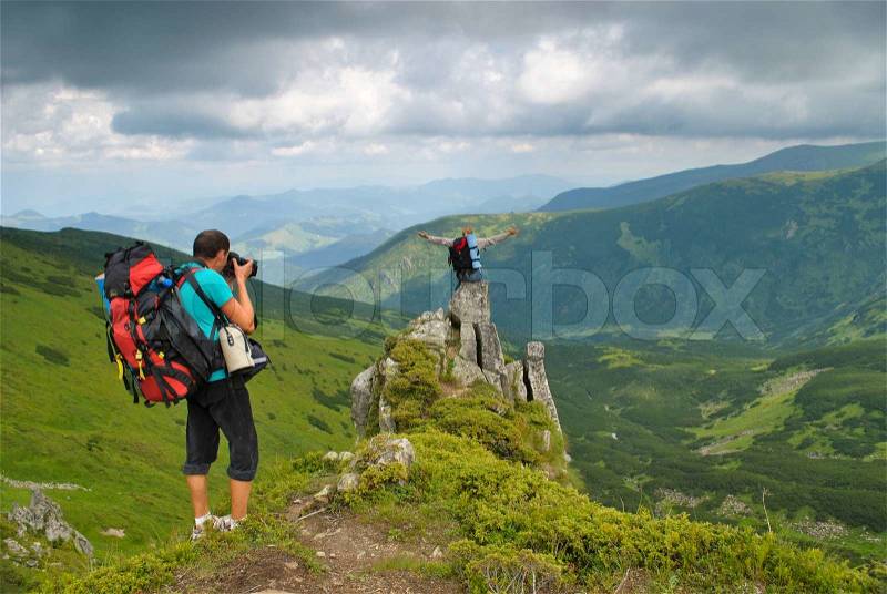 Man in montains is photographing the woman on rock with back pack, stock photo