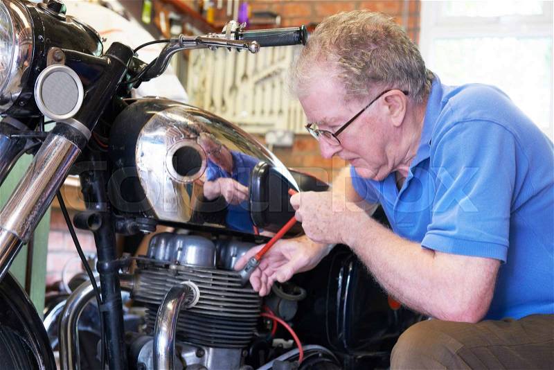 Senior Man Working On Vintage Motorcycle In Garage, stock photo